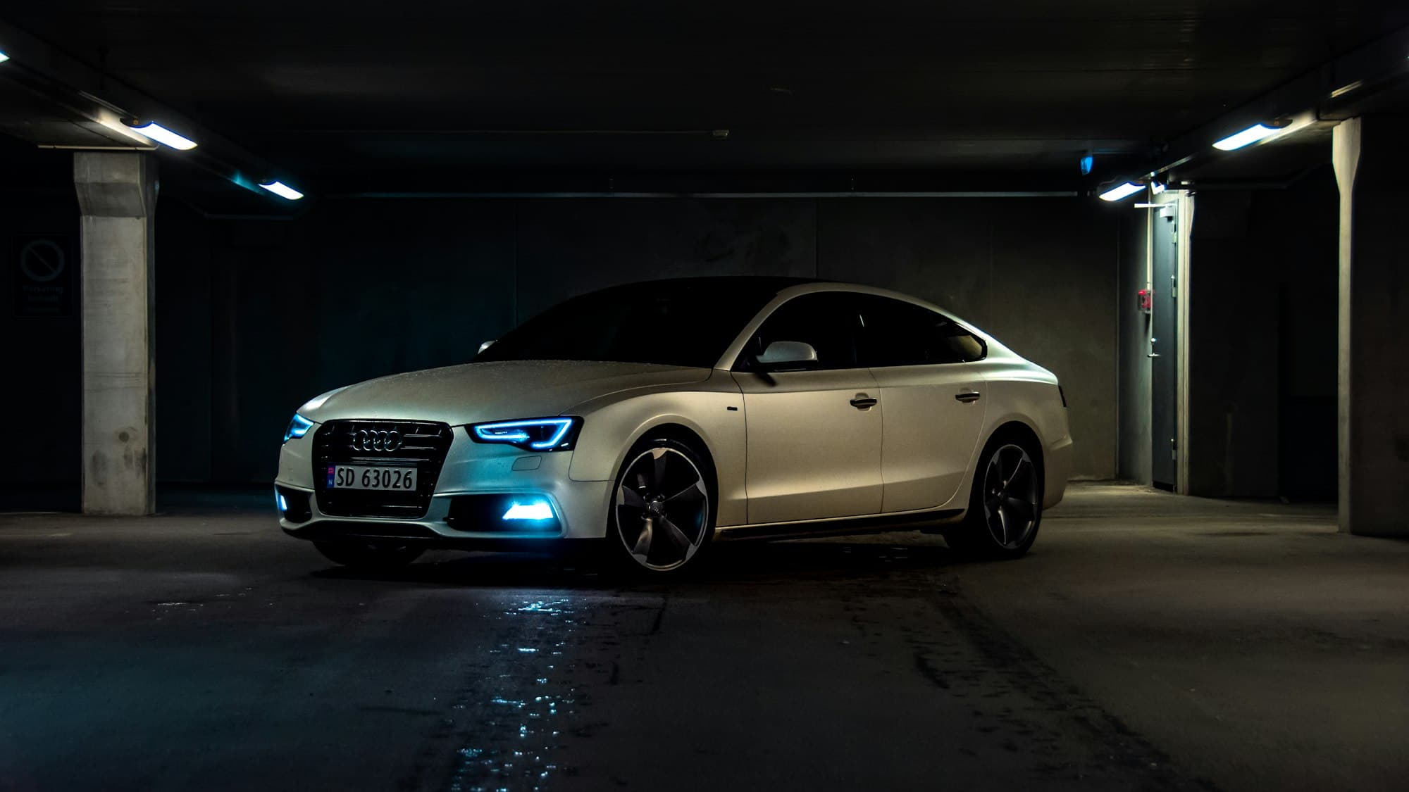 Berline blanche dans un parking souterrain, phares allumés